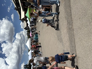 Families and children gather outdoors near colorful vendor tents; several strollers and a small child play on a paved street.